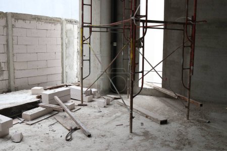 Foto einer Mauer, die aus Ziegeln gebaut wird, die mit Zement und Gerüsten in einem im Bau befindlichen Gebäude angeordnet und gemischt sind