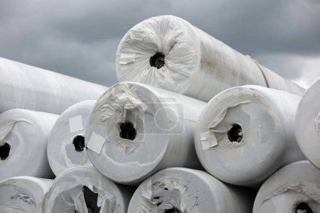 Relleno y rollos de membrana geotextil apilados y envasados en plástico blanco. Se utiliza en la construcción para aislamiento, impermeabilización y protección del sitio. Ideal para renovaciones, sótanos, lofts y paisajismo.