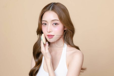 Photo for Young Asian beauty woman curly long hair with korean makeup style touch her face and perfect skin using puff on isolated beige background. Facial treatment, Cosmetology, plastic surgery. - Royalty Free Image