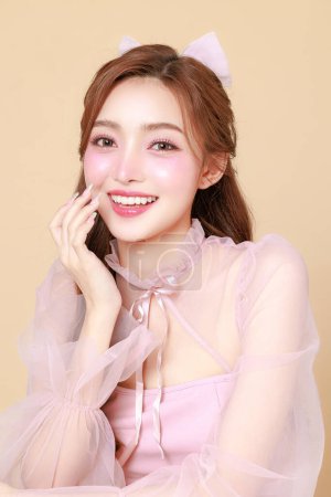 Foto de Mujer asiática linda joven en un vestido elegante rosa, maquillaje de estilo coreano, piel hidratada, lisa, perfecta sobre un fondo beige. Tratamiento facial, Cosmetología, cirugía plástica. - Imagen libre de derechos