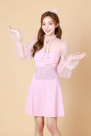 Foto de Mujer asiática linda joven en un vestido elegante rosa, maquillaje de estilo coreano, piel hidratada, lisa, perfecta palma abierta de la mano con espacio de copia sobre un fondo beige. Tratamiento facial, Cosmetología. - Imagen libre de derechos