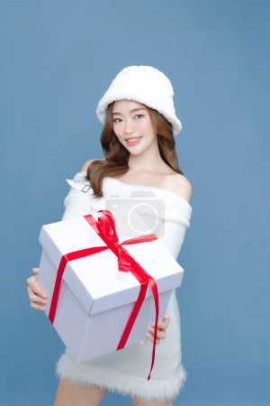 Téléchargez les photos : Jeune femme de beauté asiatique cheveux longs bouclés avec chapeau blanc et robe ont une peau propre parfaite tenant boîtes-cadeaux sur fond bleu isolé. Traitement du visage, cosmétologie, chirurgie plastique. - en image libre de droit