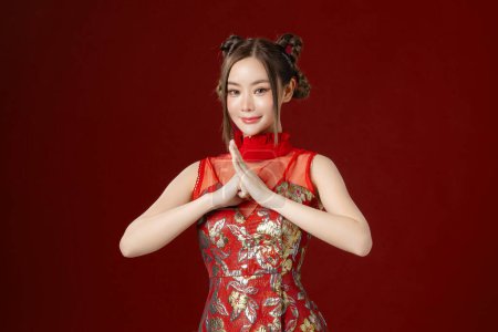 Téléchargez les photos : Belle jeune femme asiatique avec une peau propre et fraîche portant la robe traditionnelle cheongsam qipao posant sur fond rouge. Portrait de mannequin femme en studio. Bonne année chinoise. - en image libre de droit