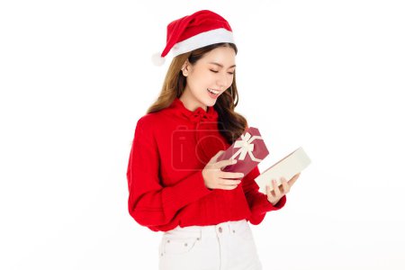 Foto de Alegre atractiva mujer asiática con un vestido rojo con un sombrero de Santa es la celebración de una caja de regalo sobre fondo blanco aislado. Hermosa dama con el pelo largo y negro. - Imagen libre de derechos