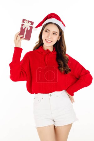 Foto de Alegre atractiva mujer asiática con un vestido rojo con un sombrero de Santa es la celebración de una caja de regalo sobre fondo blanco aislado. Hermosa dama con el pelo largo y negro. - Imagen libre de derechos