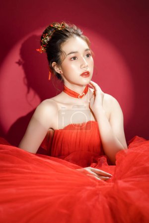 Foto de Joven modelo de mujer bonita asiática en un elegante vestido rojo de lujo sobre un fondo rojo aislado. Hermosa mujer confiada posando y mirando hacia otro lado. - Imagen libre de derechos