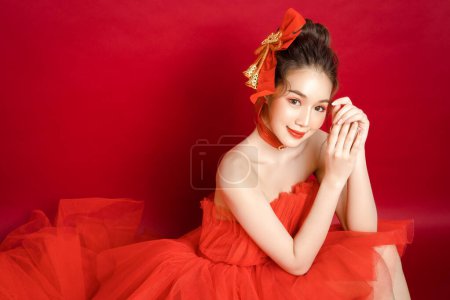 Téléchargez les photos : Jeune modèle asiatique jolie femme dans une élégante robe rouge de luxe chic sur un fond rouge isolé. Belle femme confiante posant et regarder la caméra. - en image libre de droit