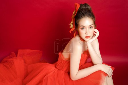 Foto de Joven modelo de mujer bonita asiática en un elegante vestido rojo de lujo sobre un fondo rojo aislado. Hermosa mujer confiada posando y mirar a la cámara. - Imagen libre de derechos