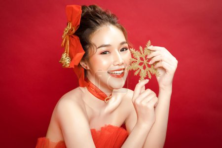 Junge asiatische hübsche Frau Modell in einem noblen stilvollen roten Luxuskleid auf rotem Hintergrund isoliert. Schöne selbstbewusste Frau posiert und schaut in die Kamera.