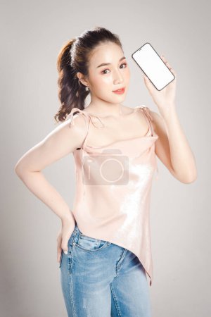 Beautiful young Asian woman is happy holding mobile phone in her hand isolated on grey banner background. 