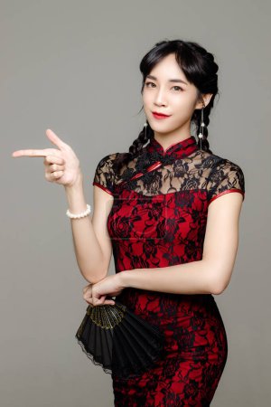 Téléchargez les photos : Bonne année chinoise. Femme asiatique portant moderne cheongsam qipao robe tenant un ventilateur sur fond isolé. Modèle féminin mignon. - en image libre de droit