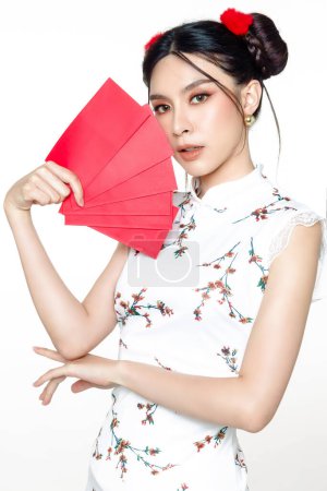 Téléchargez les photos : Bonne année chinoise. Belle femme asiatique portant traditionnelle cheongsam qipao robe regarder caméra tenant angpao ou rouge paquet cadeau monétaire isolé sur fond blanc. - en image libre de droit