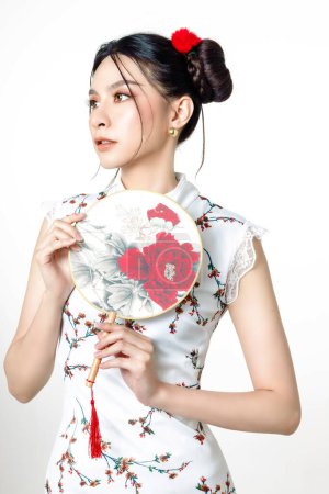 Foto de Feliz año nuevo chino. Hermosa mujer asiática vistiendo tradicional cheongsam qipao vestido con gesto de felicitación sosteniendo ventilador aislado sobre fondo blanco. - Imagen libre de derechos