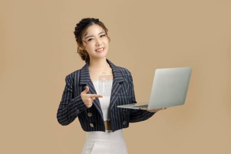 Foto de Sonríe hermosa mujer de negocios asiática sosteniendo y señalando a una tableta sobre fondo beige aislado. mirar a la cámara, copiar espacio. - Imagen libre de derechos
