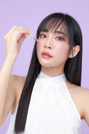 Photo for Beautiful young Asian woman model long hair with natural makeup on face clean skin apply serum on isolated violet background. Cute girl portrait, Facial treatment, Body care, Beauty and Spa. - Royalty Free Image