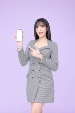 Photo for Young Asian happy woman model wearing a black and white dress is holding a blank screen cell phone and pointing to it. Portrait of businesswoman - Royalty Free Image