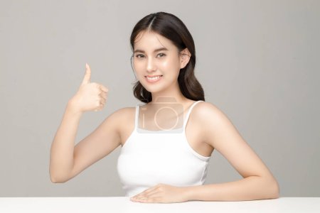 Photo for Beautiful young Asian woman model showing like thumb up with perfect clean fresh skin on grey background. Face care, Facial treatment, Cosmetology, Plastic Surgery, Lovely girl portrait in studio. - Royalty Free Image