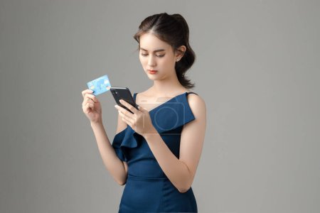Young Sad Asian woman holding credit card with blank screen mobile phone on gray background. Portrait of pretty girl in studio. cashless society Concept.