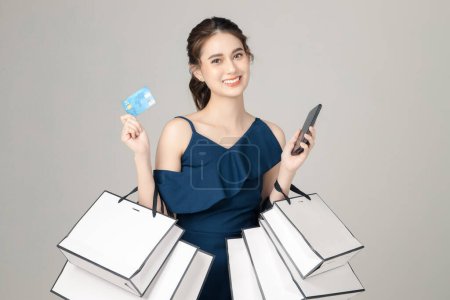 Photo for Young energetic Asian woman holding credit crad, mobile phone with shopping bags on gray background. Portrait of pretty girl in studio. cashless society Concept. - Royalty Free Image