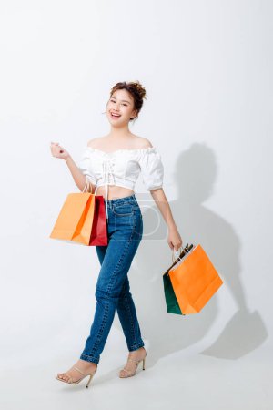 Foto de Hermosa mujer asiática de moda sosteniendo bolsas de compras de pie aislado sobre fondo blanco y espacio de copia. Compras pago en línea. sonrisa buen humor. - Imagen libre de derechos