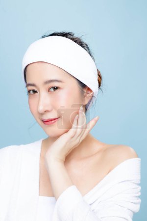 Photo for Asian woman in bathrobe with perfect clear skin. Happy girl model with fresh hydrated facial and natural makeup on isolated blue background. Cosmetology, beauty and spa, wellness, Plastic surgery. - Royalty Free Image