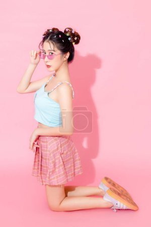 Téléchargez les photos : Portrait de belle jeune femme asiatique heureuse en bleu robe de mode mignonne porter des lunettes de soleil souriant et posant sur fond de couleur rose pastel isolé espace vide. - en image libre de droit