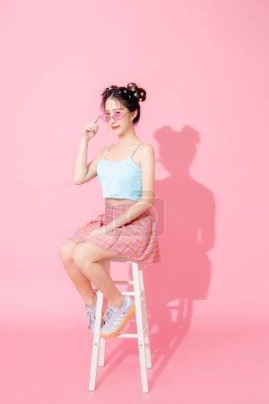 Photo for Portrait of beautiful young Asian happy woman in blue cute fashion dress wear sunglass smiling and posing on isolated pastel pink color background empty space. - Royalty Free Image