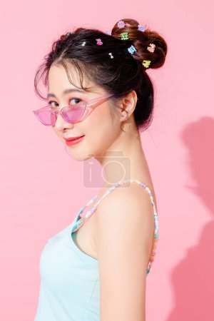 Téléchargez les photos : Portrait de belle jeune femme asiatique heureuse en bleu robe de mode mignonne porter des lunettes de soleil souriant et posant sur fond de couleur rose pastel isolé espace vide. - en image libre de droit