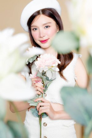 Photo for Cute Asian woman with perfect skin and holding pastel flower. Pretty girl model wearing white beret and natural makeup on beige background. Cosmetology, beauty and spa, wellness, Plastic surgery. - Royalty Free Image