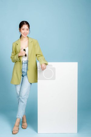 Photo for Young happy smiling successful employee business woman 20s in casual green fashion jacket stand near blank screen isolated on pastel blue background. Female entrepreneurs or office worker concept. - Royalty Free Image