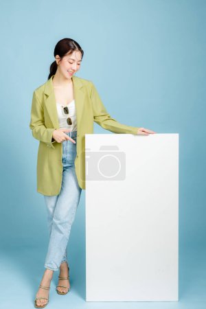 Photo for Young happy smiling successful employee business woman 20s in casual green fashion jacket stand near blank screen isolated on pastel blue background. Female entrepreneurs or office worker concept. - Royalty Free Image