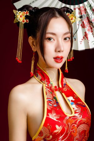 Foto de Hermosa mujer asiática con piel limpia y fresca con vestido chino tradicional sosteniendo ventilador posando sobre fondo rojo. chino feliz año nuevo. - Imagen libre de derechos