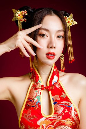 Foto de Hermosa mujer asiática con la piel limpia y fresca con vestido cheongsam qipao toque su cara en el fondo rojo. Retrato de modelo femenina en estudio. Feliz año nuevo chino. - Imagen libre de derechos