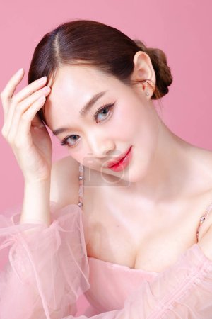 Téléchargez les photos : Belle jeune femme asiatique modèle cheveux chignon avec maquillage naturel sur le visage propre peau fraîche sur fond rose isolé. Portrait de fille mignonne, Soins du visage, Concept Valentin. - en image libre de droit