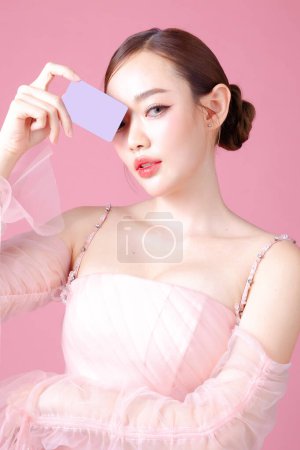 Photo for Fascinating fun joyful young woman of Asian wears sweet pink flower dress hold in hand credit bank card cover isolated on plain pastel light pink background Beautiful lady portrait in studio. - Royalty Free Image