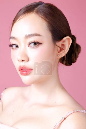 Foto de Hermosa mujer asiática modelo moño cabello con maquillaje natural en la cara limpia piel fresca sobre fondo rosa aislado. Linda chica retrato, tratamiento facial, concepto de San Valentín. - Imagen libre de derechos