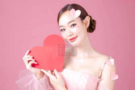 Téléchargez les photos : Attrayant jeune femme asiatique se sent heureux et romantique montrant modèle de coeur exprime des sentiments tendres pose sur fond rose. L'affection des gens et concept de soins. - en image libre de droit