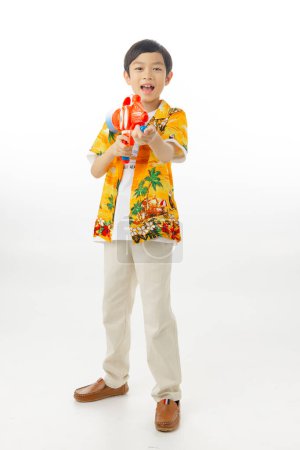 Foto de Joven atractivo niño asiático feliz sostener pistola de agua en camisas hawaianas sobre fondo blanco con camino de recorte. Songkran Tailandia. - Imagen libre de derechos