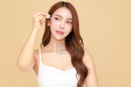 Photo for Beautiful young Asian woman model long hair using dropper for apply serum on face clean fresh skin on isolated beige background. Cute girl portrait, Facial treatment, Body care, Beauty and Spa. - Royalty Free Image