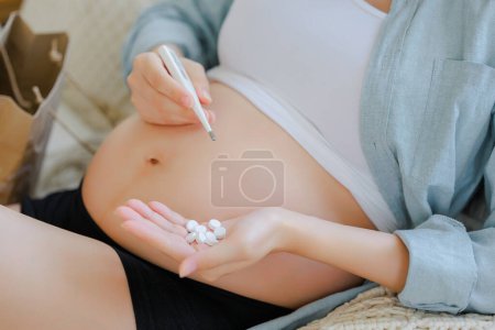 Photo for Young Asian happy pregnant woman with medicine, vitamins on bed and touching her belly. Family plan, pregnancy, motherhood, people and expectation, child and Maternity prenatal care concept. - Royalty Free Image