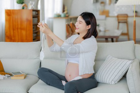Photo for Young Asian happy pregnant woman is sitting and relaxing on bed and touching her back pain. Family plan, pregnancy, motherhood, people and expectation concept - Royalty Free Image