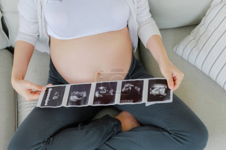 Photo for Close up crop Asian pregnant woman is and holding ultrasound 4d scan image touching her belly. Family plan, pregnancy, motherhood, people and expectation, child and Maternity prenatal care concept. - Royalty Free Image