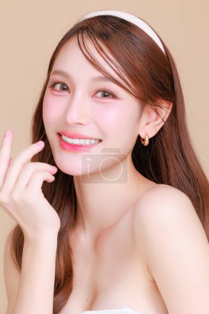 Téléchargez les photos : Jolie beauté asiatique femme cheveux longs bouclés avec maquillage coréen visage éclatant et visage sain portrait de la peau sourire sur fond beige isolé. Cosmétologie, Chirurgie plastique. - en image libre de droit