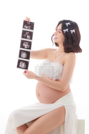 Téléchargez les photos : Joyeux jeune asiatique enceinte avec maquillage coréen sur le visage et la peau parfaite Mère avec échographie de son bébé à naître. sur fond blanc isolé. Concept de grossesse, Soins prénatals de maternité. - en image libre de droit