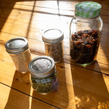 Foto de Semillas en frascos de vidrio en una encimera de cocina de madera con luz solar que fluye sobre ellos. Enfoque selectivo. - Imagen libre de derechos