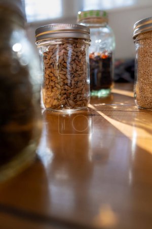Foto de Semillas en frascos de vidrio en una encimera de cocina de madera con luz solar que fluye sobre ellos. Enfoque selectivo. - Imagen libre de derechos