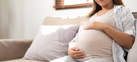 Foto de Embarazo, descanso, personas y concepto de expectativa - primer plano de la feliz mujer embarazada sonriente y tocándose el vientre en casa. - Imagen libre de derechos