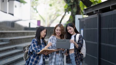 Foto de Nice young students use laptop after class sitting outdoors. girls wear casual clothes in spring. Concept of modern education. - Imagen libre de derechos