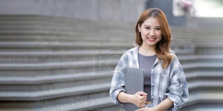 Téléchargez les photos : Asiatique étudiante avec son ordinateur portable devant le bâtiment du campus. - en image libre de droit