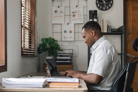 Foto de Hombre africano que trabaja con computadora portátil en casa mientras está sentado. Sobre el hombro cerca de la vista de pantalla simulada.. - Imagen libre de derechos